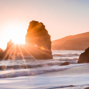 View of rocks jutting up in the ocean with the sunset behind them.